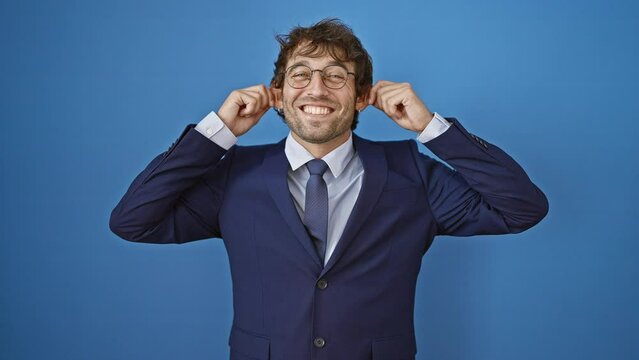Young man wearing business suit smiling pulling ears with fingers, funny gesture. audition problem over isolated blue background