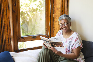 A mature biracial woman reading a magazine at home, with copy space