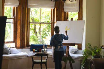 A mature biracial woman artist paints on a canvas at home, with copy space