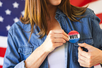 A middle-aged caucasian woman pins a vote badge on her denim shirt