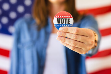 A caucasian woman is holding out a vote badge towards the camera, with copy space unaltered