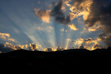 Sun light rays shining through dark clouds over mountains.