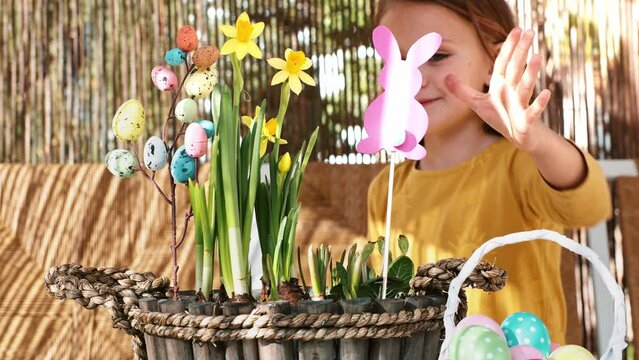 Happy child girl make spring Easter composition with yellow flowers, paper colored Easter bunny, eggs basket. Children prepare decoration present for Easter party at home. Kid creativity and hobby DIY