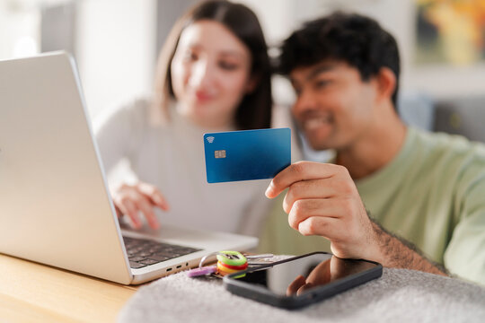 Happy couple engaged in an online purchase, with the man holding a credit card and the woman typing on a laptop
