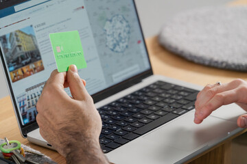Close-up of a man's hand holding a green credit card over a laptop, finalizing an online payment