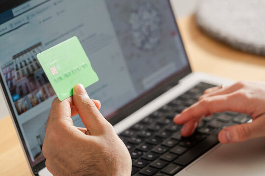 Close view of a man's hands holding a green credit card and using a laptop, processing a secure online payment