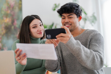 A young man captures an image of a paper document using his smartphone, with a focused expression as a woman looks on. The scene suggests a moment of sharing information or digitizing paperwork