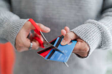 A man's hands cutting a blue credit card with red scissors, symbolizing financial management or the end of a credit account. The decisive cut reflects personal finance decisions