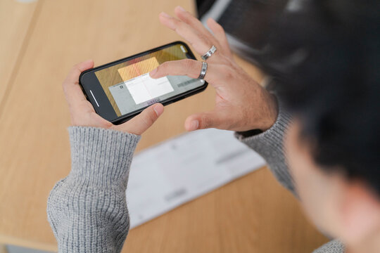 Close-up image of a smartphone in a man's hands, displaying a scanned bill on the screen. It highlights the use of mobile technology for online payment