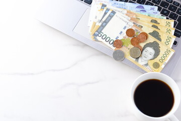 韓国の通貨、ウォンKRW（紙幣と硬貨）とノートパソコン、コーヒーの入ったコーヒーカップ
