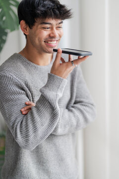 A cheerful young man in a grey sweater engages in a lively conversation over his smartphone, his demeanor reflecting ease and friendliness