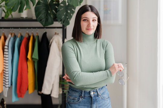 Woman in green turtleneck sweater stands with arms crossed, exuding confidence and style in a plant-filled room