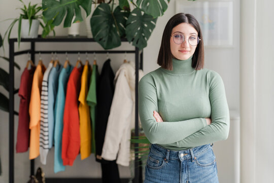 Woman in green turtleneck sweater stands with arms crossed, exuding confidence and style in a plant-filled room