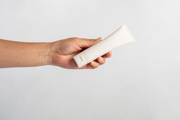 Female hand holds cosmetic product in tube, bottle, lotion or serum on white background.