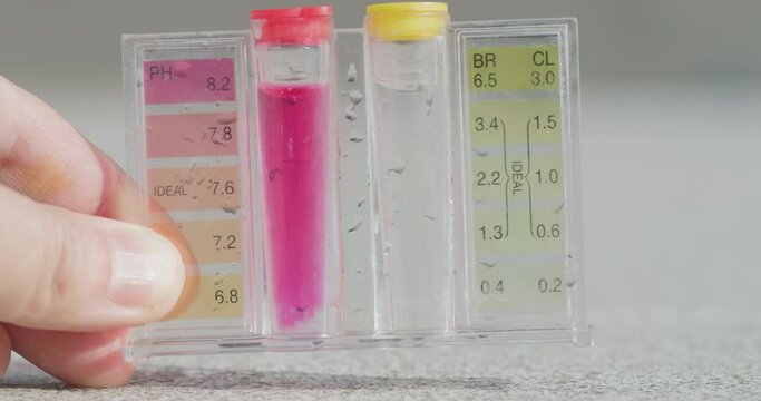 A hand holds a test tube with tests for PH and chlorine levels.