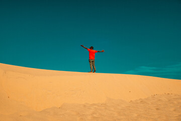A man with arms outstretched standing on a sand dune at Mambrui Sand dunes in Mambrui beach in Malindi, Kenya 