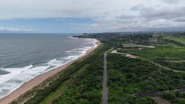 Aerial of the beach at famous divers paradise Aliwal Shoal Beach near Scottburgh, South Africa, a white SUV drives down a rural highway