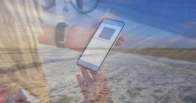 Composition of woman holding a smartphone with qr code on screen against aerial view of the beach