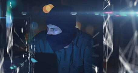 Image of digital interface with data processing over male hacker in balaclava using laptop