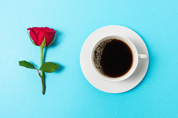 Creative composition of red rose flower and cup of coffee on blue background. Minimal spring concept.