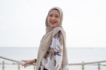 Pretty muslim woman enjoying sun shine at the beach wearing cardigan.