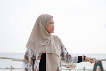 Pretty muslim woman enjoying sun shine at the beach wearing cardigan.