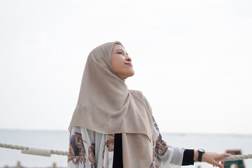 Pretty muslim woman enjoying sun shine at the beach wearing cardigan.