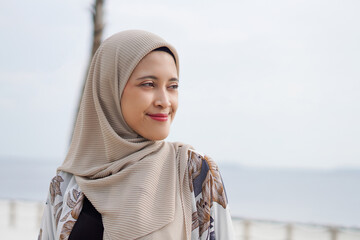 Pretty muslim woman enjoying sun shine at the beach wearing cardigan.