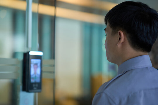 Person using facial recognition machine for access lobby door.