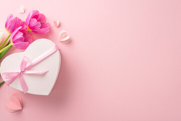 Ideal Women's Day scene: top view showcasing a heart-shaped present adorned with a bow, love symbols, and a bunch of tulips on a pale pink backdrop, space for text included