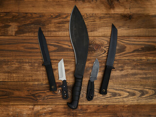 Close-up of five different fixed-blade knives laid out on the brown wooden background. Black and...