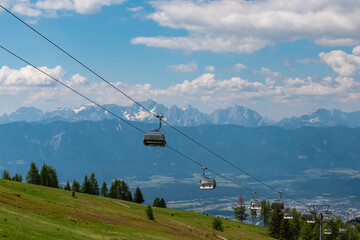 Ski lift in summer with scenic view of majestic mountain range Julian Alps seen from Gerlitzen, Carinthia, Austria. Wanderlust in Austrian Alps. Idyllic hiking trail along alpine meadow and forest