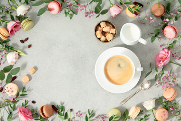 Fototapeta na wymiar White cup of coffee and Frame made of Spring flowers and different types of macaroons