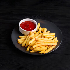 French fries with tomato sauce. on a black wooden background.