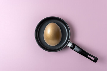 Gold egg in small frying pan on pastel pink background. Minimal food concept.