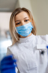 Young female doctor or nurse in medical mask and gloves holds test tube with blood sample in her hands.
