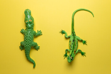 Green crocodile toy and lizard toy on bright yellow background. Minimal art concept.