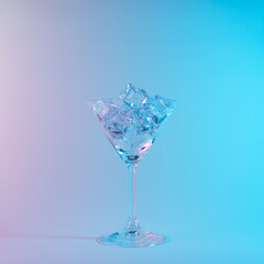 Martini glass with ice cubes in neon holographic vibrant pink and blue colors. Minimal celebration concept.