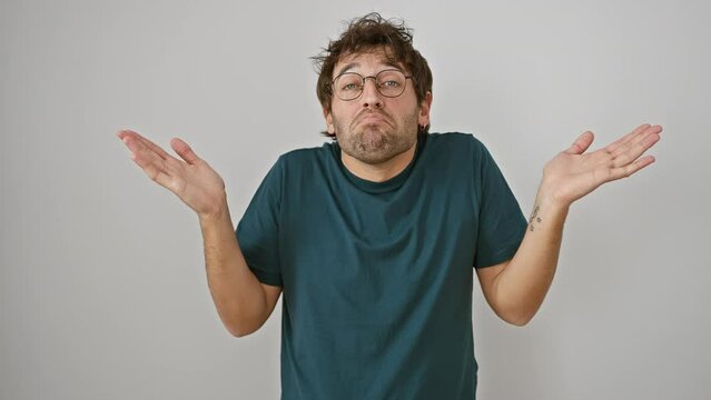 Puzzled young hispanic man in glasses, arms raised in a clueless shrug. lost in ambiguous emotion, standing against isolated white background.