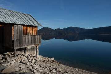 A quaint and weathered wooden shack nestled on the serene shore of a shimmering lake, offering rustic charm.