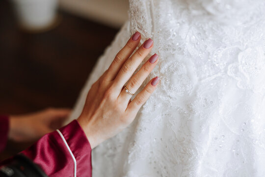 morning portrait of a luxurious and beautiful bride in a hotel in a luxurious room in red pajamas standing next to her wedding dress.