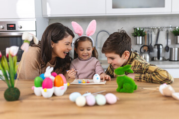 Mother, son and daughters are painting eggs. Happy family are preparing for Easter. Cute little...