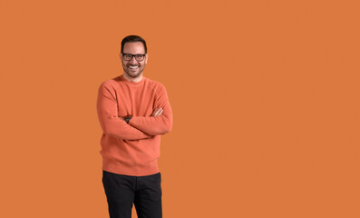 Portrait of smiling confident young businessman with arms crossed standing over orange background