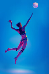 Fototapeta na wymiar Dynamic portrait woman, sportsman, volleyball player training to hits ball in mid-air against gradient blue background in pink neon light. Concept of sport games, movement, active, healthy lifestyle.
