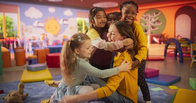 Portrait of an Attractive Happy Young Teacher Hugging with Young Cute Kids in a Modern Colorful Kindergarten Room. Female Educator Taking Care of Happy Active Multiethnic Children in Daycare