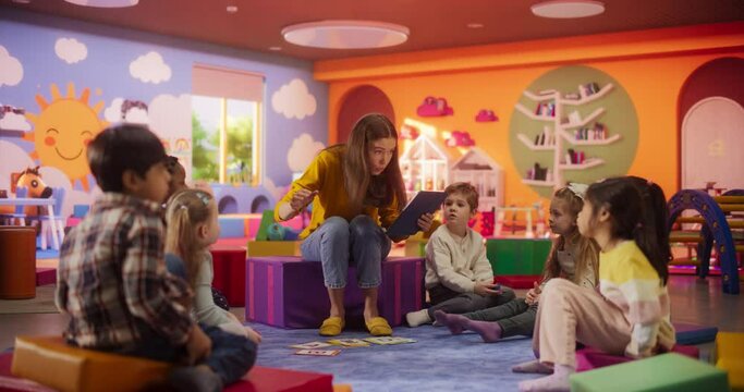 Beautiful Daycare Teacher Using a Tablet Computer to Tell an Educating Story for Young Talented Kids. Female Educator Having Fun Supervising Diverse Group of Small Boy and Girls