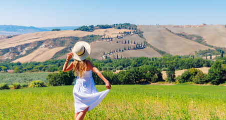 A girl in a white dress on a green field in italian Tuscany- Val d'Orcia
