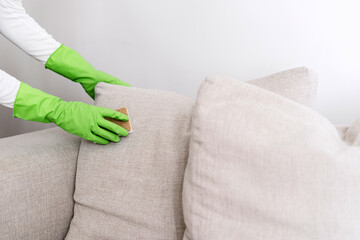Cropped shot of female hands in gloves hold sponge and cleaning couch cushion