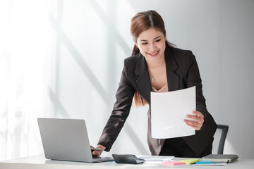 Asian Business woman using calculator and laptop for doing math finance on an office desk, tax,...