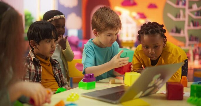 Cute Caucasian, Asian and African Kids Playing Together with Colorful Building Blocks. Smart Adorable Children Using Laptop Computer to Watch Educational Videos and Tutorials for Building Toy Castles